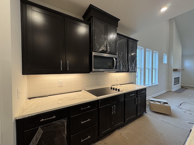 kitchen with dark cabinetry, stainless steel microwave, black electric stovetop, and backsplash