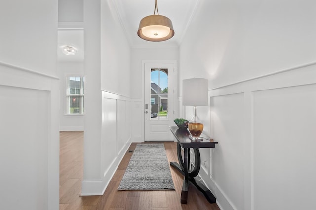 entrance foyer featuring wainscoting, wood finished floors, crown molding, and a decorative wall