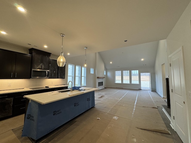 kitchen with a center island with sink, lofted ceiling, a sink, light countertops, and stainless steel microwave