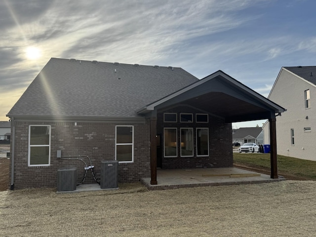 back of house featuring a patio area, cooling unit, a shingled roof, and brick siding