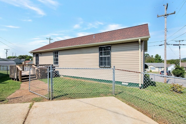 rear view of house with fence, roof with shingles, a deck, a yard, and a gate