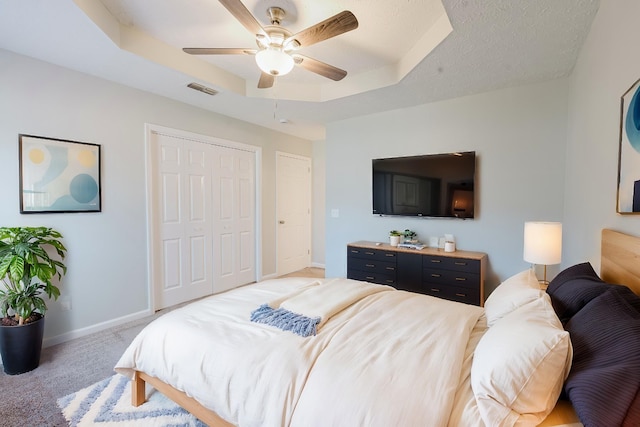 bedroom featuring visible vents, baseboards, light colored carpet, a tray ceiling, and a ceiling fan