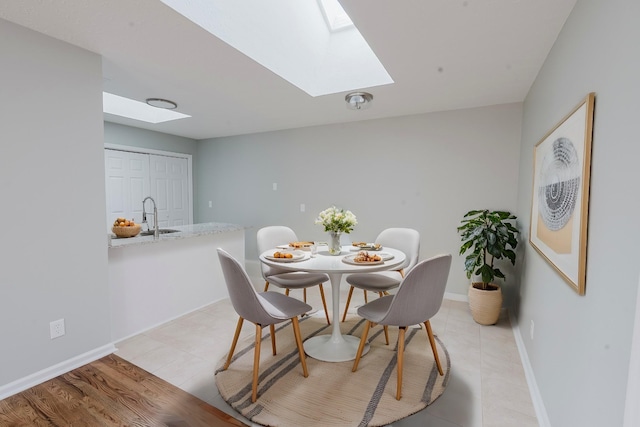 dining space with light wood finished floors, a skylight, and baseboards