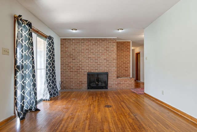 unfurnished living room featuring baseboards, a brick fireplace, and wood finished floors