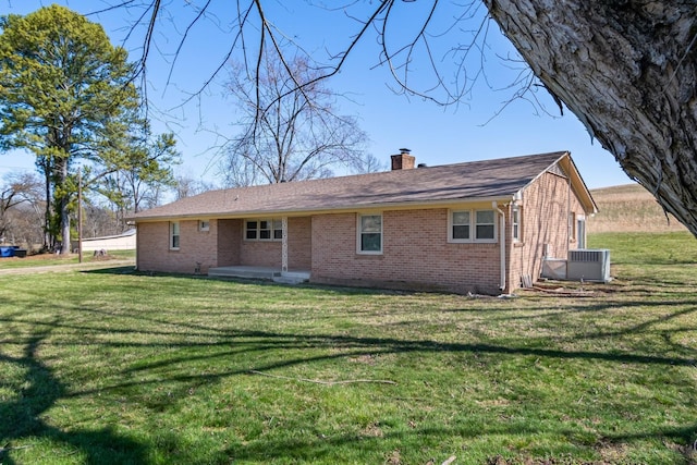 rear view of property with brick siding, central air condition unit, a chimney, and a yard