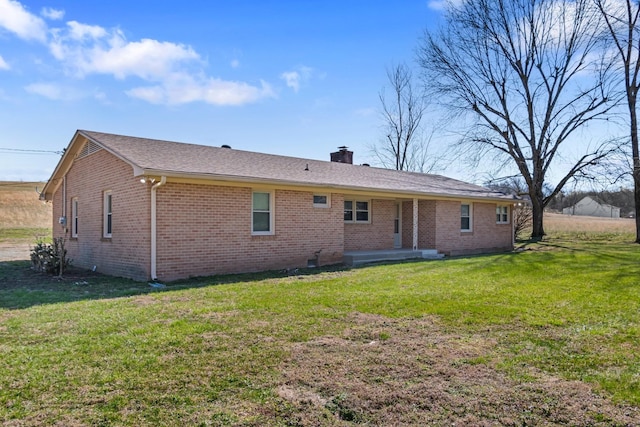 back of house with brick siding, a chimney, and a yard