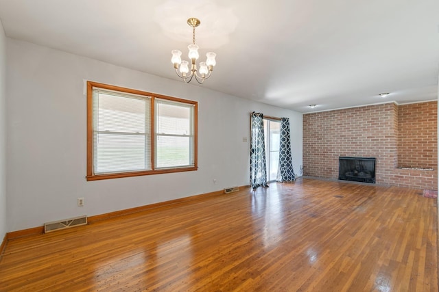 unfurnished living room featuring visible vents, hardwood / wood-style floors, an inviting chandelier, a fireplace, and baseboards