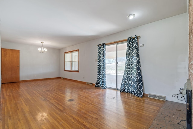 unfurnished room featuring a chandelier, visible vents, baseboards, and wood finished floors