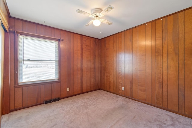 unfurnished room with visible vents, carpet floors, wood walls, and a ceiling fan