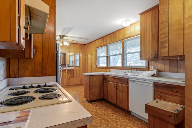 kitchen with wooden walls, light countertops, white appliances, a ceiling fan, and a sink