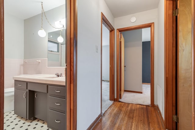 hallway featuring tile walls, light wood-style floors, and a sink