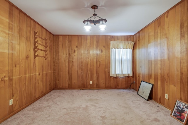 carpeted spare room with wood walls and an inviting chandelier