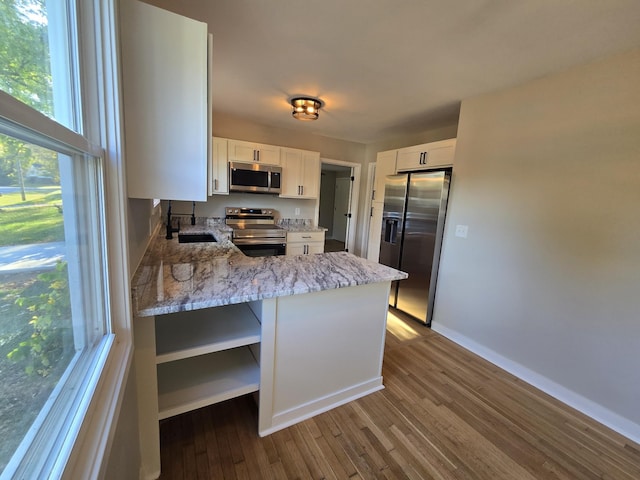 kitchen featuring a peninsula, dark wood-style flooring, a sink, stainless steel appliances, and white cabinetry