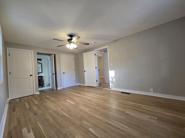 unfurnished bedroom with visible vents, connected bathroom, baseboards, and wood finished floors