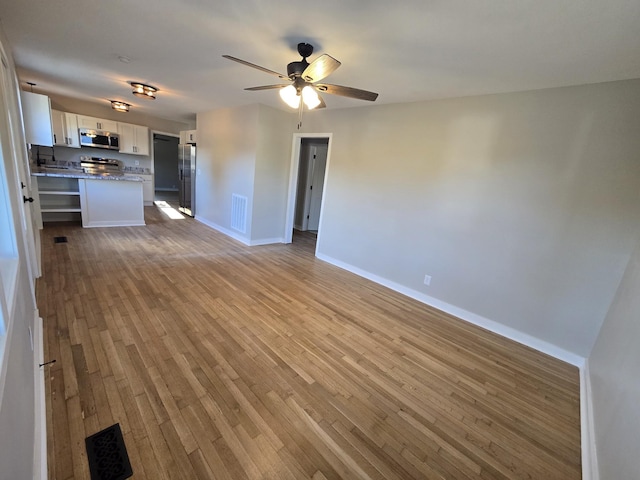 unfurnished living room featuring visible vents, a ceiling fan, baseboards, and wood finished floors