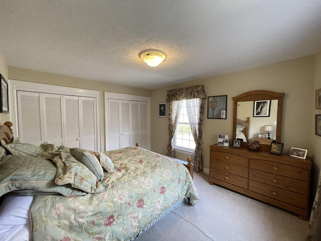 bedroom with light carpet, two closets, and a textured ceiling