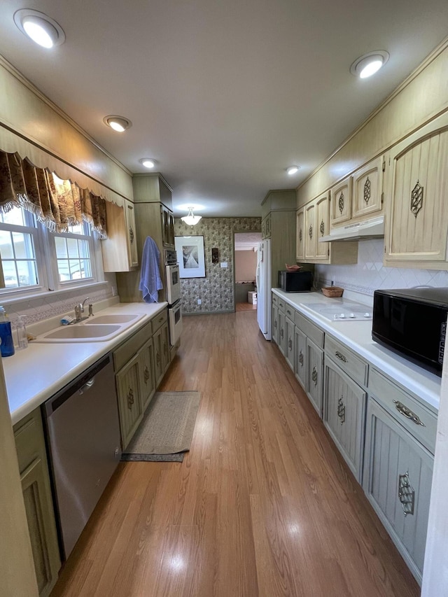 kitchen featuring light wood-type flooring, a sink, wallpapered walls, stainless steel appliances, and light countertops