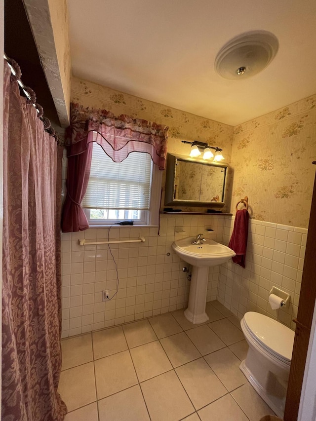 bathroom featuring a wainscoted wall, wallpapered walls, tile patterned floors, toilet, and tile walls