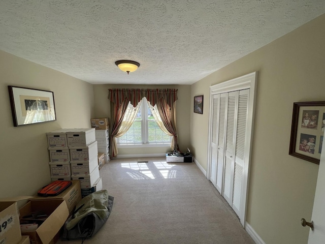 bedroom featuring baseboards, light carpet, a textured ceiling, and a closet