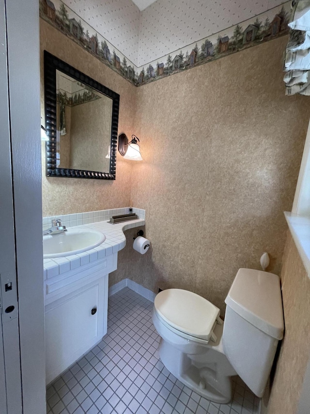 half bathroom featuring tile patterned flooring, toilet, wallpapered walls, and vanity