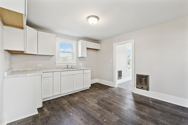 kitchen featuring dark wood-type flooring, a sink, heating unit, white cabinetry, and baseboards