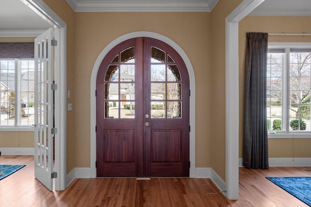 foyer with wood finished floors, french doors, arched walkways, crown molding, and baseboards