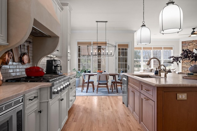 kitchen featuring light wood finished floors, crown molding, decorative backsplash, appliances with stainless steel finishes, and a sink