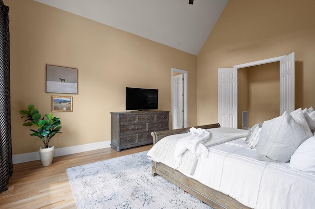 bedroom with visible vents, high vaulted ceiling, baseboards, and wood finished floors