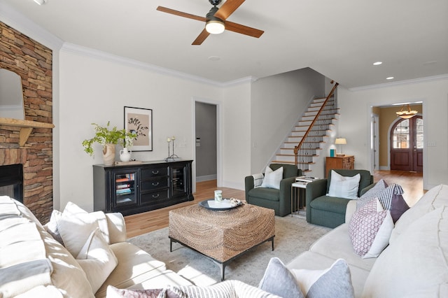 living room with ceiling fan with notable chandelier, wood finished floors, stairway, crown molding, and baseboards