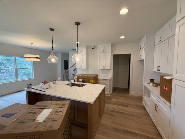 kitchen with a sink, an island with sink, wood finished floors, and white cabinets