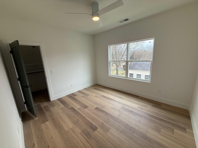 unfurnished bedroom with visible vents, a walk in closet, ceiling fan, baseboards, and wood finished floors