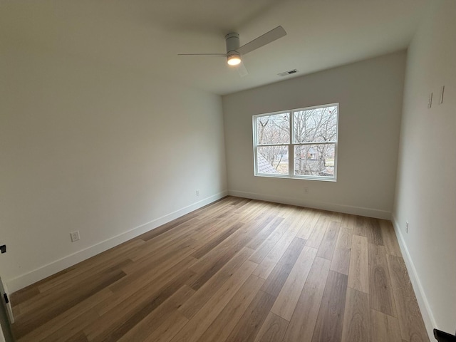 spare room featuring a ceiling fan, visible vents, wood finished floors, and baseboards