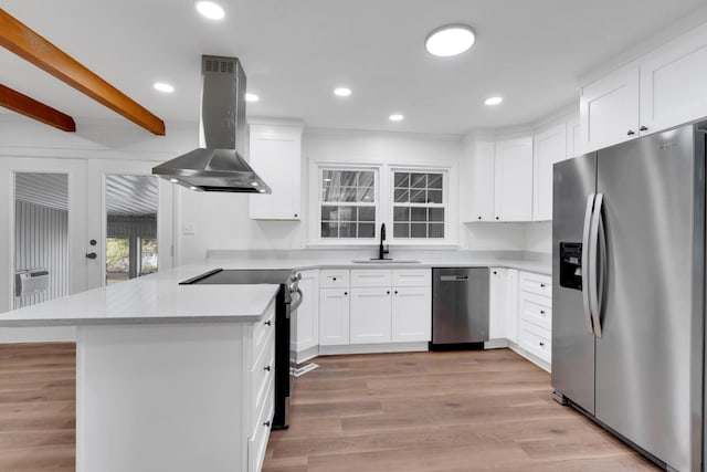 kitchen featuring light wood finished floors, a peninsula, island exhaust hood, a sink, and stainless steel appliances