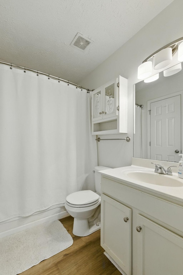 full bathroom featuring visible vents, toilet, a textured ceiling, wood finished floors, and vanity