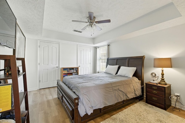 bedroom featuring baseboards, visible vents, light wood finished floors, ceiling fan, and a textured ceiling