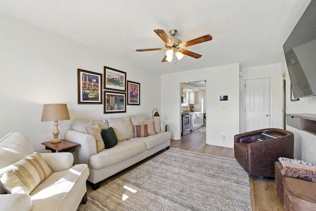 living area with a ceiling fan, light wood-type flooring, and a textured ceiling