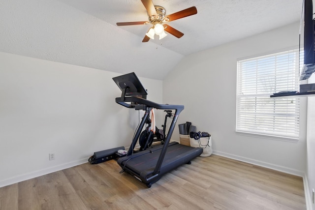 workout area featuring wood finished floors, baseboards, ceiling fan, vaulted ceiling, and a textured ceiling