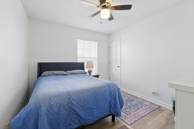 bedroom featuring a textured ceiling, a ceiling fan, baseboards, and wood finished floors