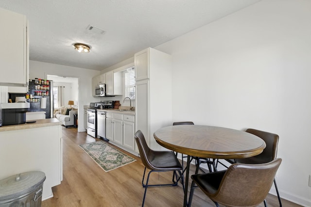 dining room with a textured ceiling, baseboards, visible vents, and light wood-type flooring