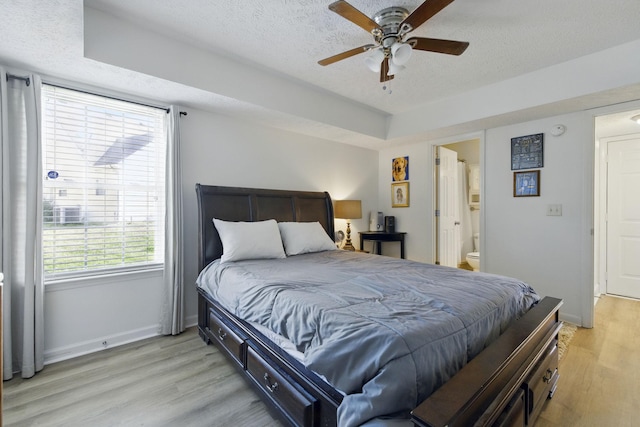 bedroom featuring baseboards, light wood-style floors, ensuite bath, a textured ceiling, and a ceiling fan