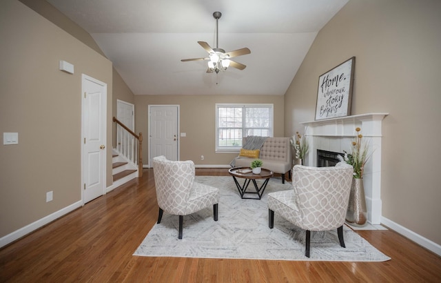 living area with a tiled fireplace, stairs, lofted ceiling, and wood finished floors