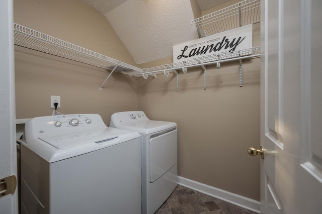 laundry area featuring baseboards, laundry area, stone finish floor, a textured ceiling, and washing machine and dryer