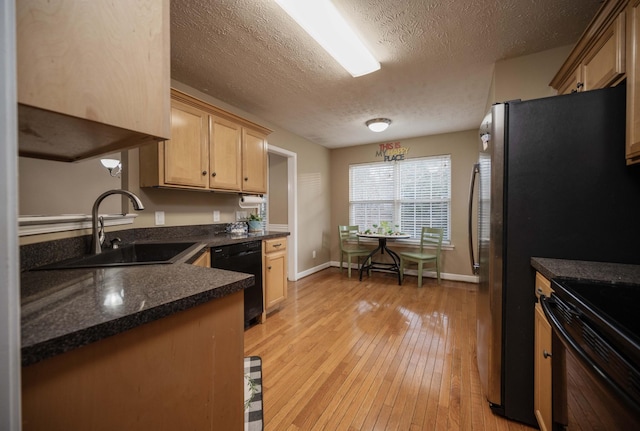 kitchen with black appliances, light wood-style flooring, a sink, dark countertops, and baseboards