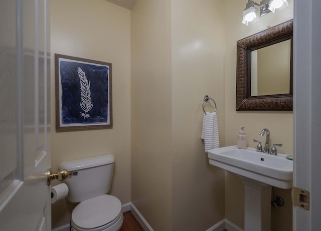 half bathroom with toilet, baseboards, and a sink