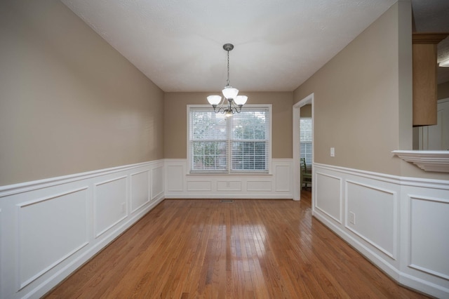 unfurnished dining area featuring a notable chandelier, light wood-style flooring, and wainscoting