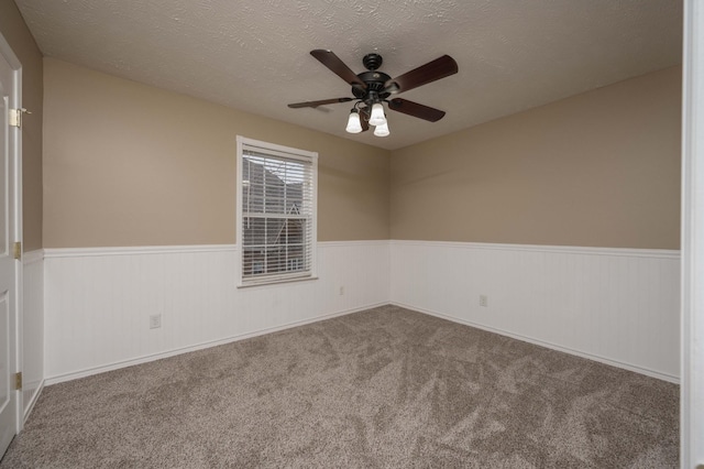 empty room with a wainscoted wall, a ceiling fan, carpet flooring, and a textured ceiling