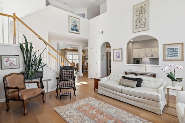 living room with baseboards, ornate columns, arched walkways, stairs, and light wood-type flooring