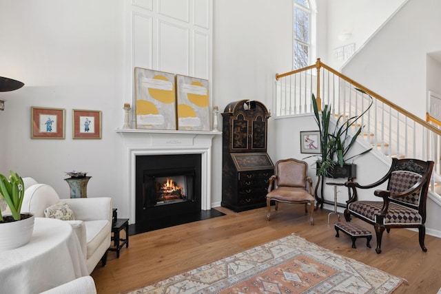 sitting room featuring light wood-type flooring, a fireplace with flush hearth, a high ceiling, and stairway