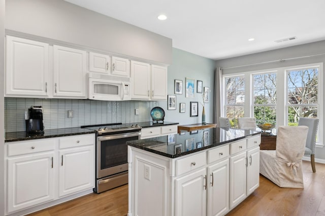 kitchen with electric range, a kitchen island, light wood-style floors, decorative backsplash, and white microwave