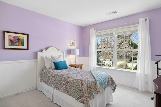 bedroom with visible vents, light carpet, and wainscoting